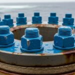 Coated industrial bolts on an offshore pipeline flange showing corrosion protection.
