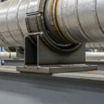 Industrial pipe shoe welded to an insulated pipeline resting on a steel support beam.