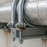 Heavy-duty steel pipe support brackets securing insulated piping in an industrial facility.
