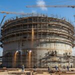 Large industrial steel storage tank under construction with cranes and scaffolding