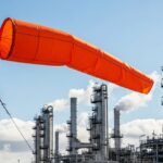 High-visibility orange wind sock blowing on a metal pole at an oil refinery.