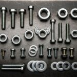 A collection of different mechanical fasteners including bolts, screws, nuts, and rivets arranged on a dark background.