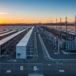 Grid-scale lithium-ion battery energy storage system facility at sunset with modular containers and substation infrastructure.