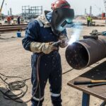 Professional welder performing high-precision field welding on industrial piping in a refinery construction site.