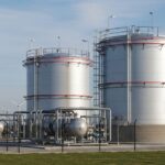 Large industrial green ammonia storage tank with cryogenic piping and renewable energy infrastructure in the background.