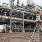 Professional land surveyor using a total station on an industrial construction site for topographical surveys.