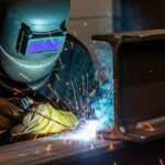 Certified welder performing structural welding repair on a heavy steel beam with sparks flying.