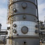 Industrial vertical pressure vessel showing shell construction and nozzle connections in a refinery setting.