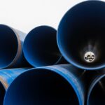 Large-diameter steel pipes with protective blue anti-corrosive epoxy coating stacked in an industrial facility.