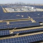 Aerial view of a utility-scale solar power plant featuring rows of photovoltaic panels and a central substation for grid connection.